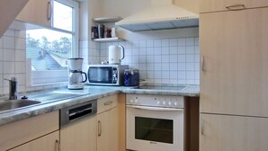 A compact kitchen with a dishwasher, microwave, coffee maker, and oven. - Ferienwohnung F18 - 2-zi. Fewo im Dachgeschoss für 3 Personen mit Wlan (Graal-Müritz)