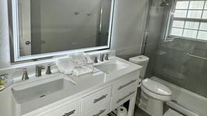 A modern bathroom with two sinks, a large mirror, and a shower.