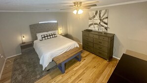 A bedroom with a bed, a bench, a dresser, a ceiling fan, and a wall art piece.