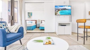 Et moderne hotelværelse med seng, fjernsyn, sofabord og udsigt til en strand.