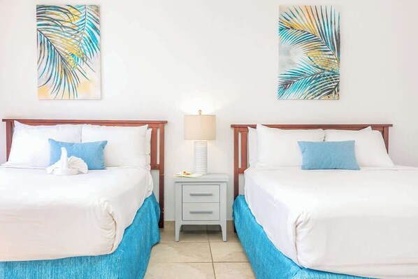 Habitación de hotel con dos camas, una mesita de noche, una lámpara y obras de arte en las paredes.