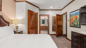 Une chambre d’hôtel avec un grand lit, des portes en bois, une salle de bain visible à travers une porte ouverte et une commode avec des tiroirs.