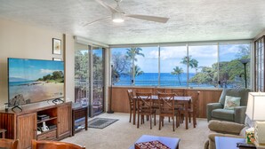 Una sala de estar con televisor grande, muebles de madera, comedor y vista al océano.