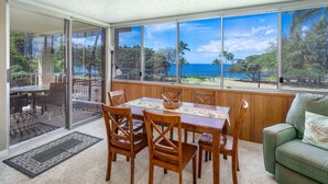 Un comedor con una mesa y sillas, vista al océano y un sofá verde.
