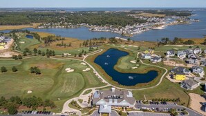 An aerial view of a golf course with a lake, surrounded by residential areas and a clubhouse. - Windswept Dr  Condo in a quiet, golf course community close to Rehoboth Beach (Millsboro)