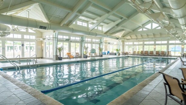 An indoor swimming pool with clear lanes, a sunlit roof, and lounge chairs along the sides. - Windswept Dr  Condo in a quiet, golf course community close to Rehoboth Beach (Millsboro)