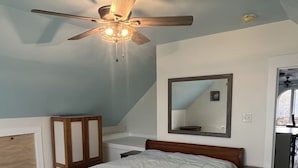 Un dormitorio con cama, ventilador de techo, mesita de noche y banco de madera.