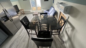 Una cocina moderna con una mesa de comedor de vidrio, sillas negras y un refrigerador de acero inoxidable.
