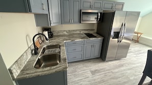 Una cocina moderna con armarios grises, un refrigerador de acero inoxidable, un microondas integrado y una encimera de mármol.