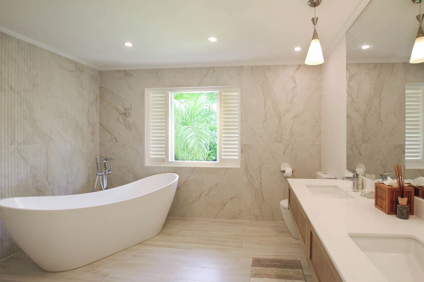 A modern bathroom with a freestanding bathtub, a large mirror, and a window with a view of greenery.