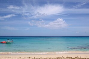 A beach with clear turquoise water, a boat, and a sandy shore.