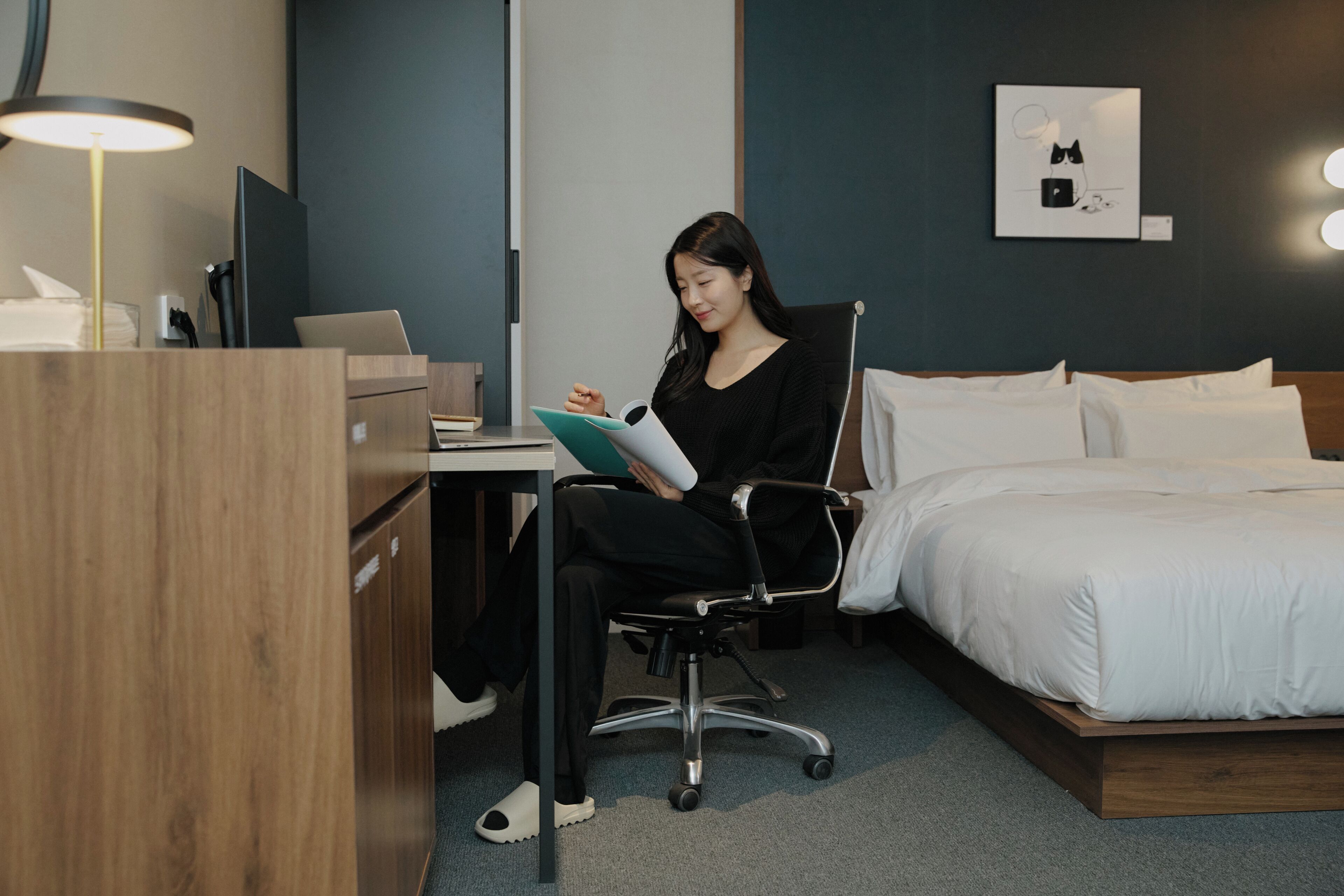 A hotel room with a bed, desk, chair, and a lamp.