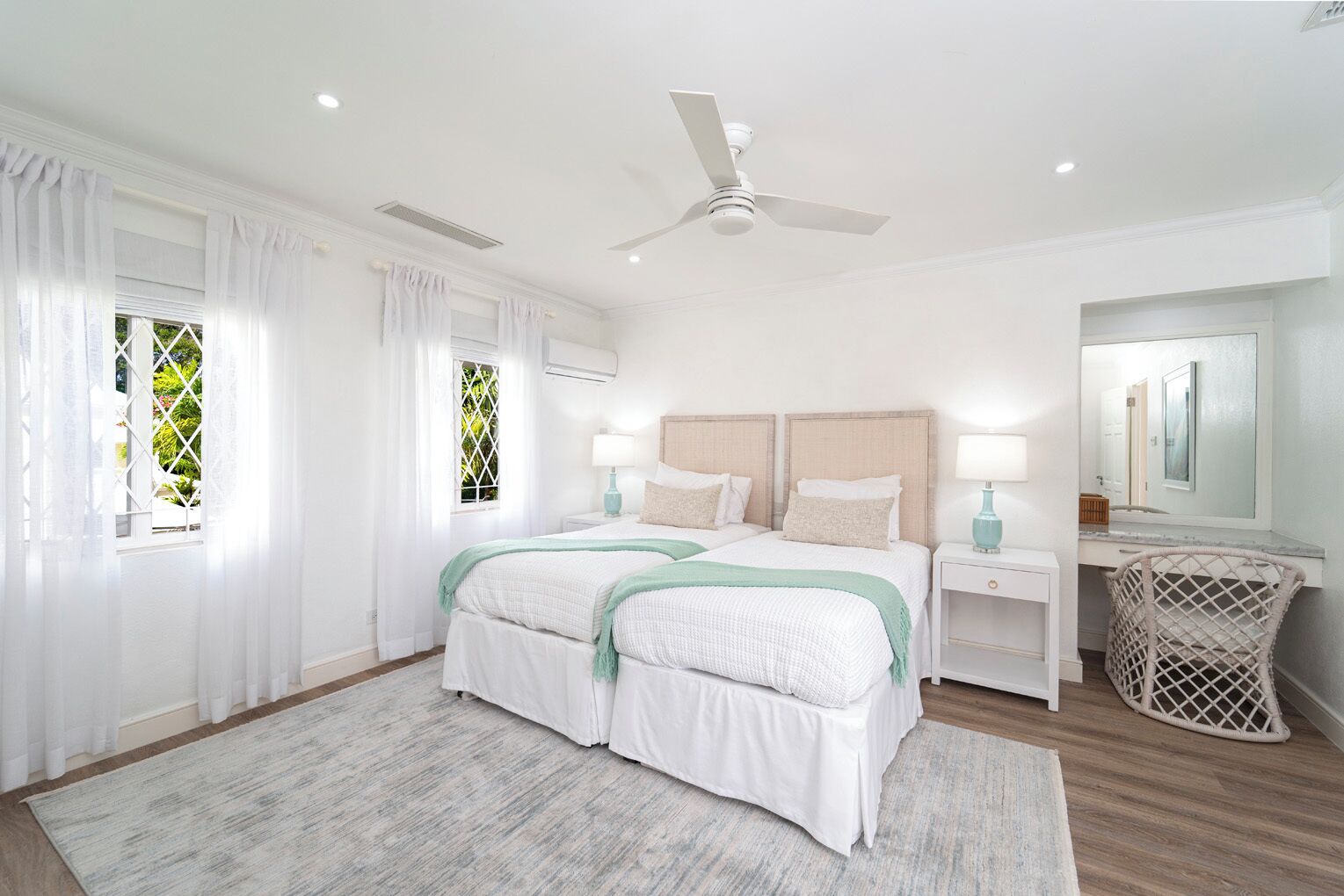A bedroom with a bed, two bedside tables, a ceiling fan, a window with curtains, and a mirror.
