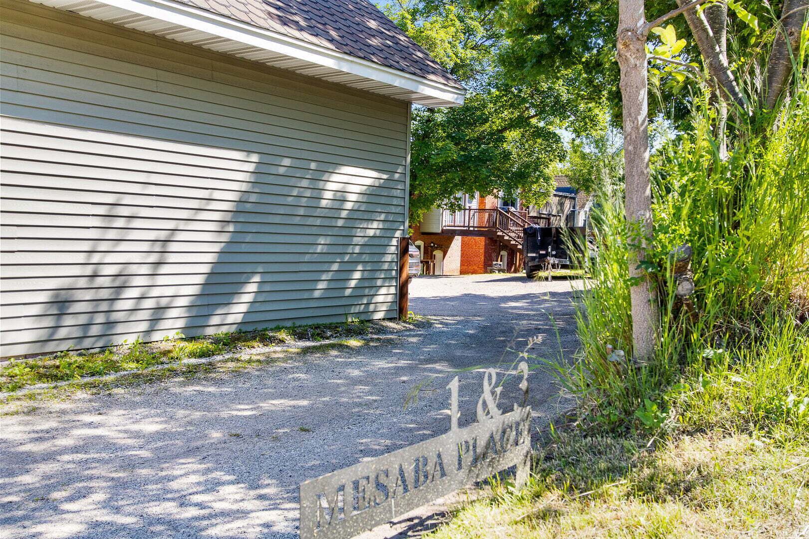 A residential property with a gravel driveway leading to a house with a covered porch.