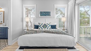 Une chambre dotée d’un grand lit, de deux tables de chevet avec des lampes, d’une œuvre d’art encadrée au-dessus du lit, et offrant une vue sur l’extérieur grâce à de grandes fenêtres.