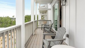 Une véranda couverte avec des balustrades blanches, deux fauteuils Adirondack, un ventilateur de plafond et une vue sur le paysage environnant.