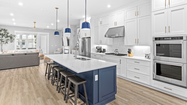 Une cuisine moderne avec des meubles blancs, un grand îlot central doté de tabourets, des appareils en acier inoxydable et des suspensions bleues.