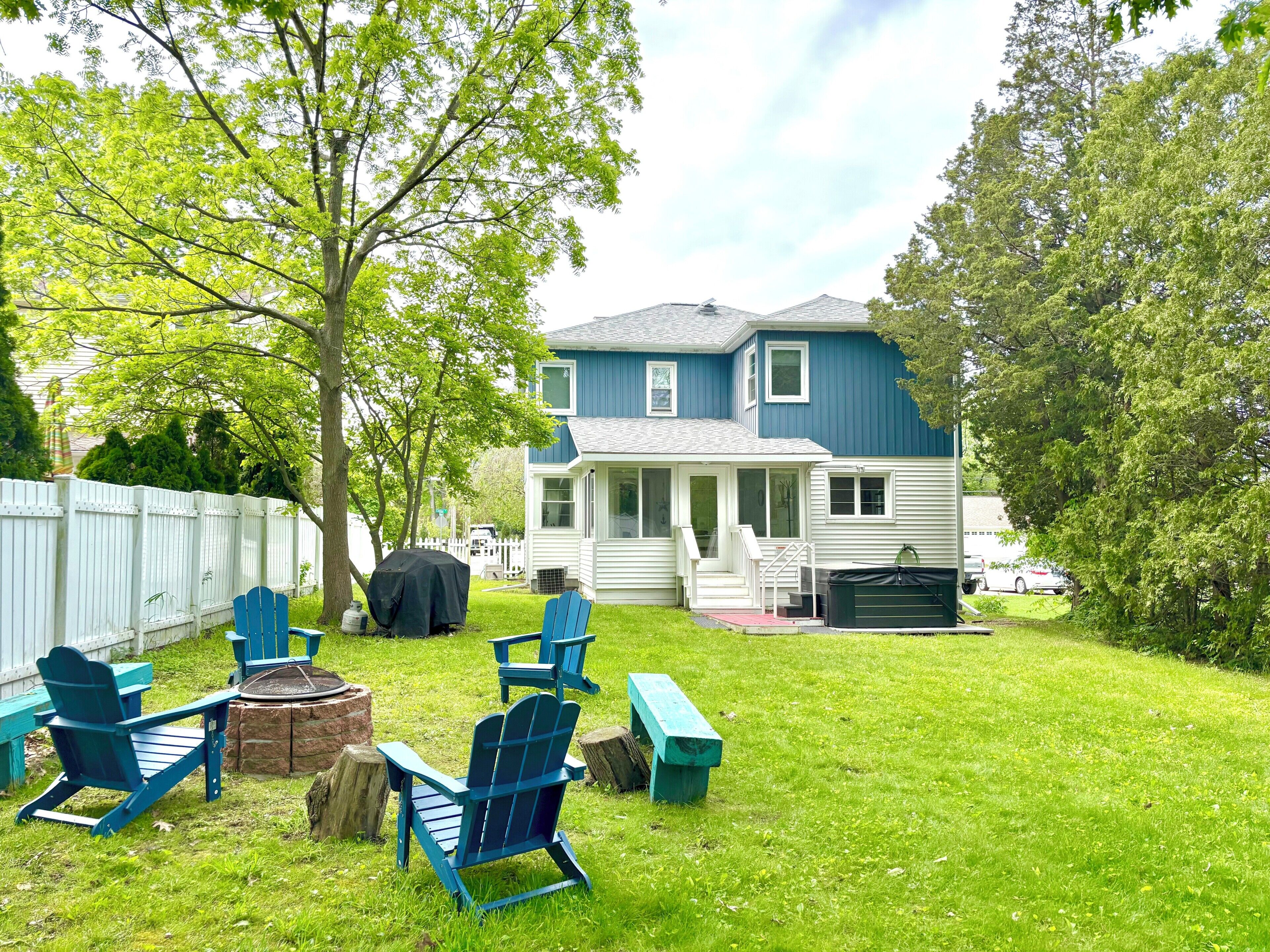 A backyard with a lawn, a covered grill, and blue Adirondack chairs.