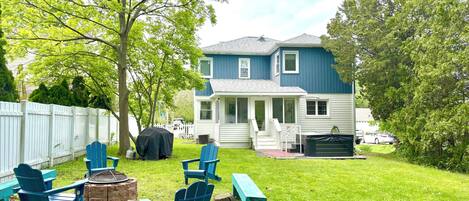 A backyard with a lawn, a covered grill, and blue Adirondack chairs.