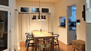 A dining area with a wooden table and chairs, a chandelier, and a view of the kitchen through an open door. - Private Raleigh Bungalow Retreat near Downtown Raleigh (Raleigh)