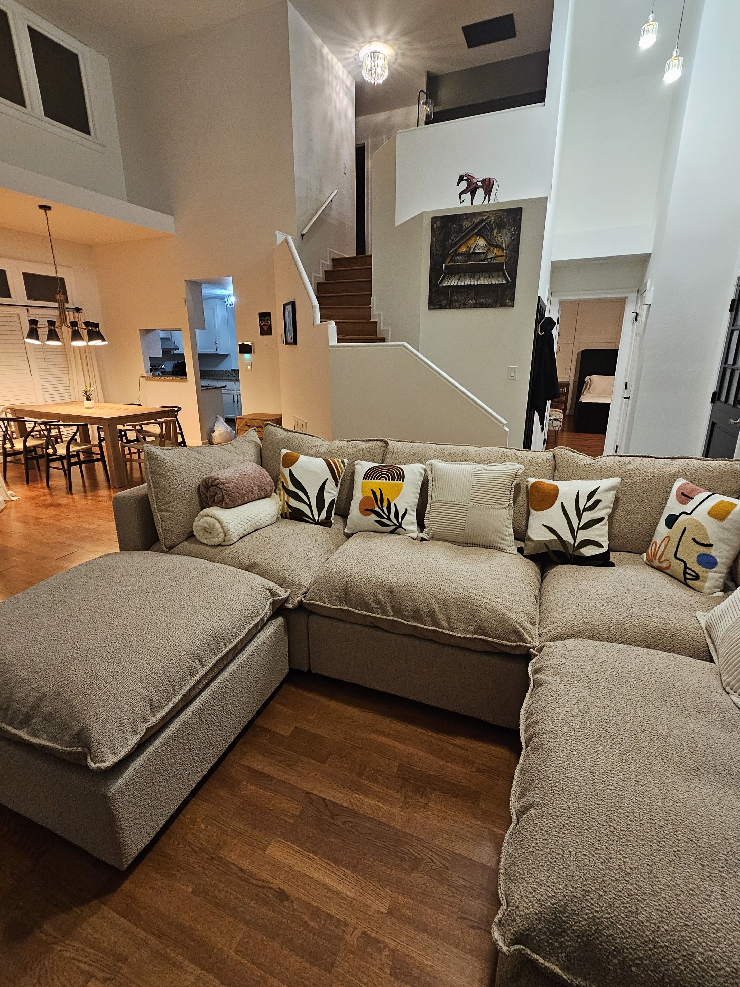 A modern living room with a sectional sofa, wooden flooring, a dining area, and a staircase leading to an upper level.
