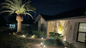 A residential property at night with a paved pathway, a palm tree, and a lit-up house number. - Golf Course View! Heated Pool - Villa Fairway to Florida - Roelens Vacations (Cape Coral)