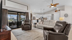 A modern living room with leather sofas, a wooden coffee table, and a TV. - Golf Course View! Heated Pool - Villa Fairway to Florida - Roelens Vacations (Cape Coral)