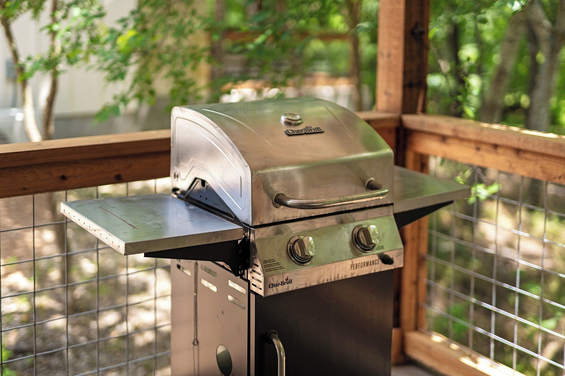Un barbecue à gaz Char-Broil doté d’un brûleur latéral et d’un couvercle, placé sur une terrasse en bois avec une rambarde en métal.