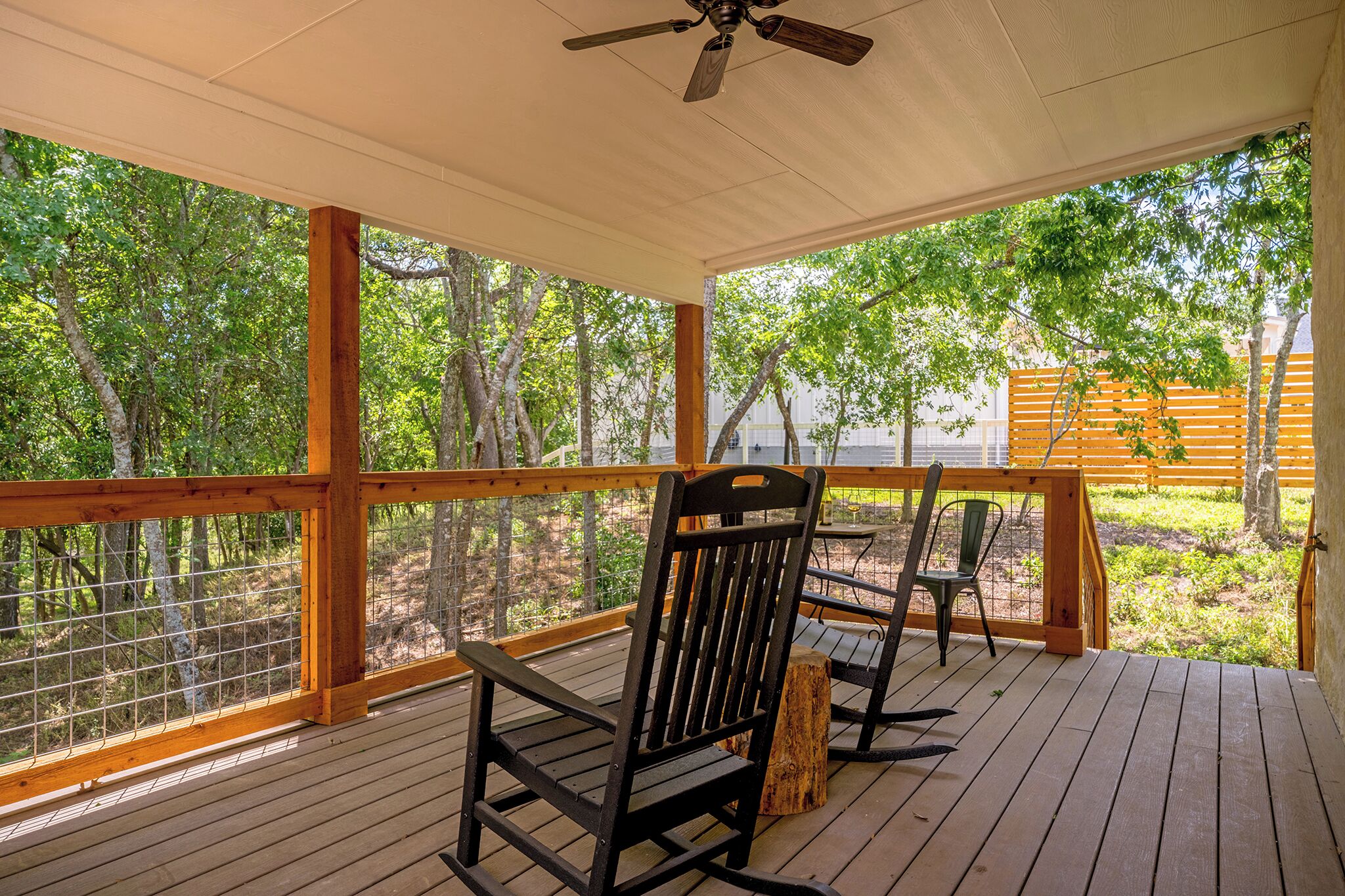 A covered porch with wooden flooring, two rocking chairs, and a ceiling fan.