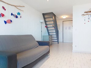Ein Wohnzimmer mit grauem Sofa, einer Holzleiter an der Wand und einem weiß gefliesten Boden.