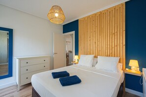 Un dormitorio con una cama grande, dos mesitas de noche con lámparas, un cabecero de madera, un aparador blanco y un espejo en la pared.