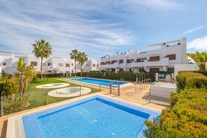 Ein modernes Hotel mit zwei Schwimmbecken, Palmen und einem gepflegten Rasen.
