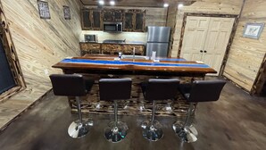 A wooden interior with a bar area featuring a long table and four bar stools.