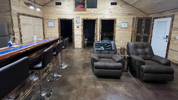 A rustic wooden interior with a bar area, seating, and a fireplace.