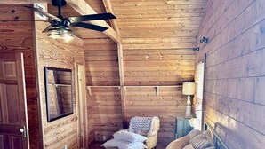 Camera da letto in una baita di legno, con un letto, una sedia, un comodino, una lampada e una ventola a soffitto.