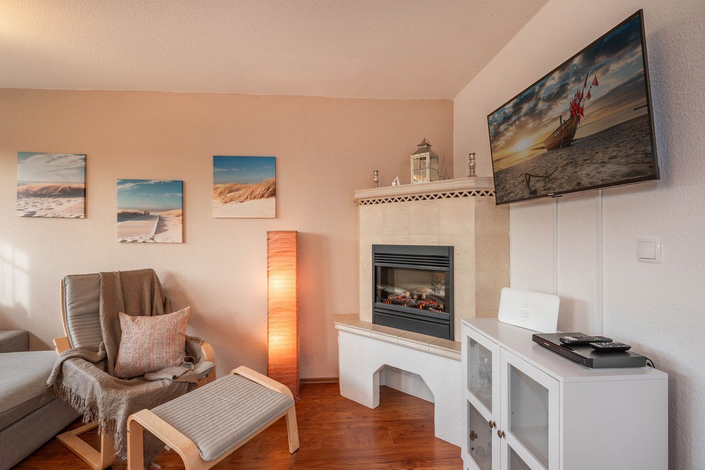 Un salon avec une cheminée, un téléviseur fixé au mur et un tableau représentant une scène de plage.