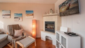 Una sala de estar con chimenea, televisor montado y un cuadro de una playa.