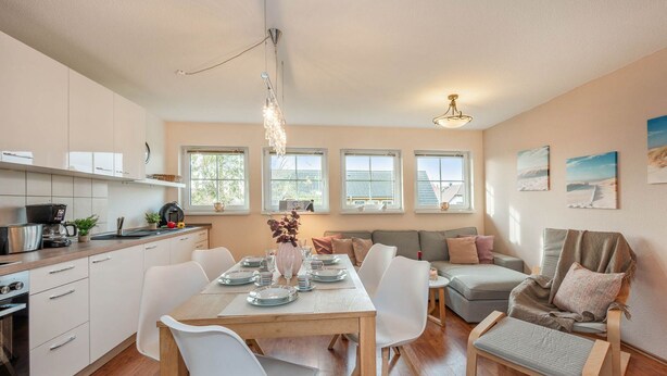 Una cocina moderna con armarios blancos, una mesa de comedor para cuatro personas y una zona de estar acogedora con un sofá y sillones.