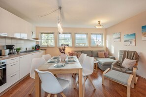 A modern kitchen with white cabinets, a dining table set for four, and a cozy seating area with a sofa and armchairs. - Strandbrise - Ferienwohnung Strandbrise (Koserow)