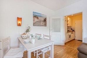 Un coin repas avec une table dressée pour deux personnes, un tableau blanc et un tableau représentant une scène de plage.