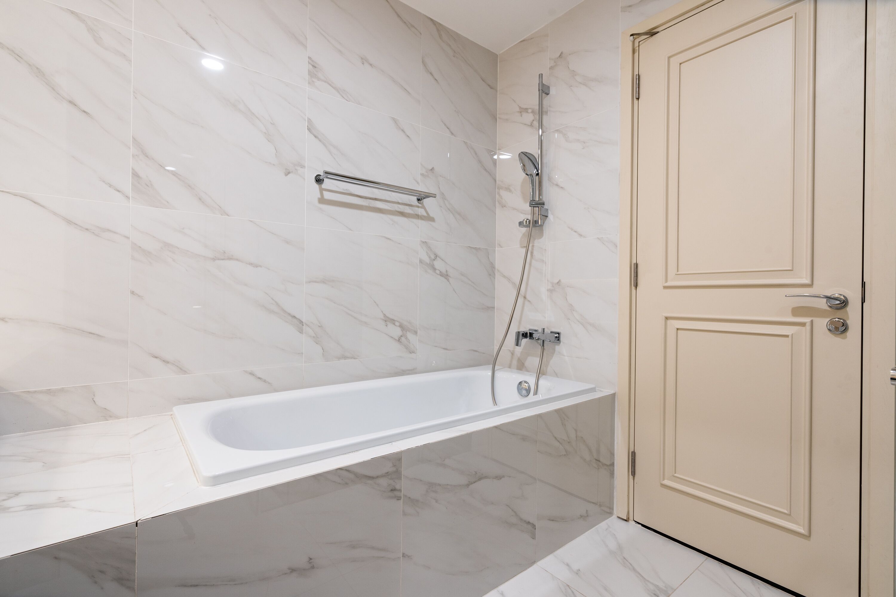A modern bathroom with a marble floor and walls, a freestanding bathtub, a showerhead, and a door.