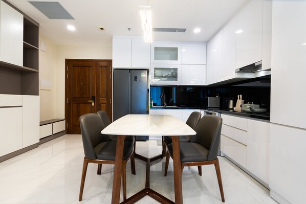 A modern kitchen with white cabinetry, a stainless steel refrigerator, and a dining table with four chairs. - Losso Central - Madison Building D1 (Ho Chi Minh City)