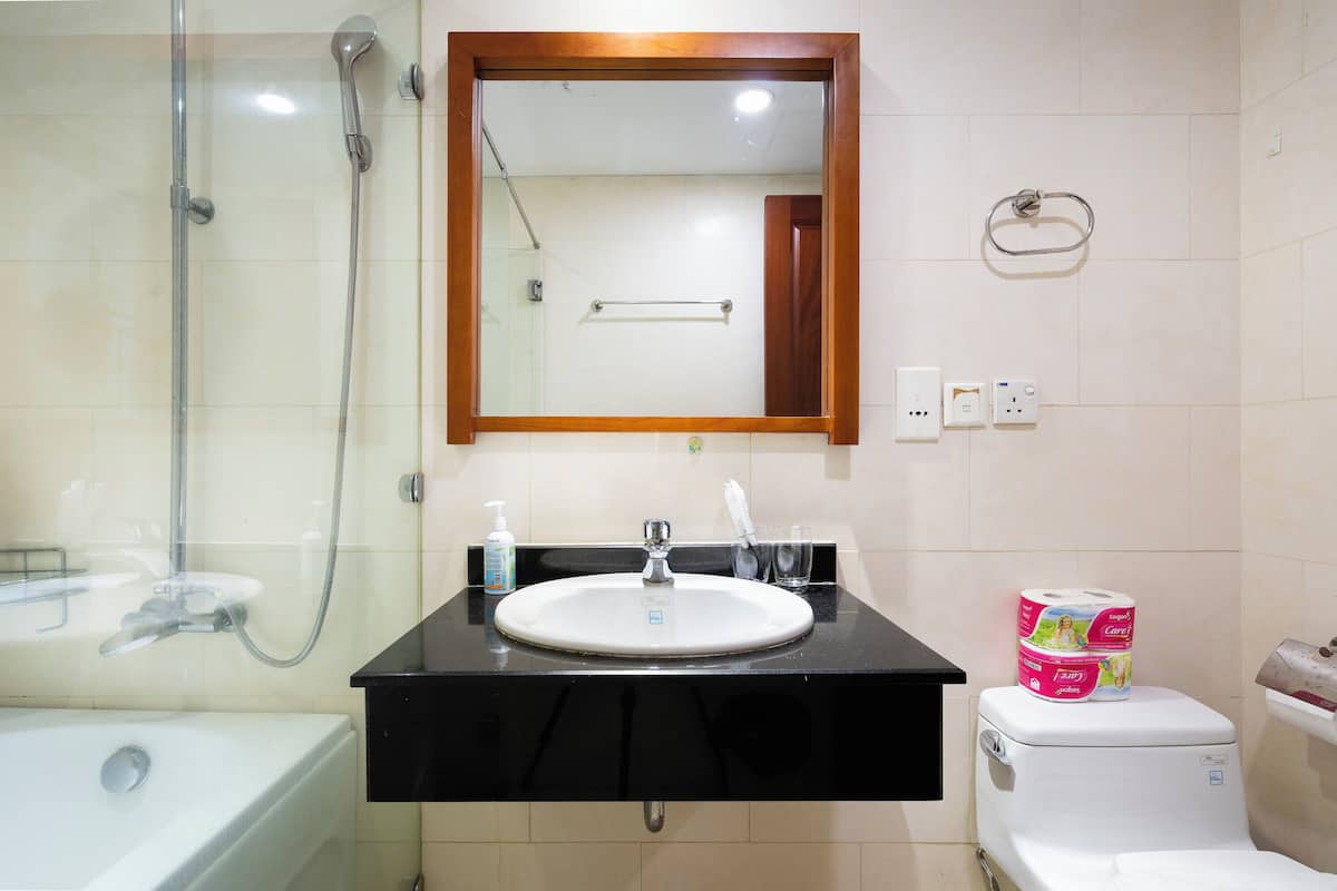 Une salle de bain équipée d’un lavabo, d’un miroir, d’une douche, de toilettes et d’un rouleau de papier toilette.