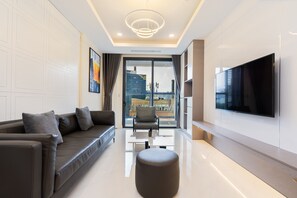 A modern living room with a sofa, ottoman, and a flat-screen TV mounted on the wall. - Losso Central - Madison Building D1 (Ho Chi Minh City)