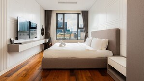 Ein modernes Hotelzimmer mit einem großen Bett, einem an der Wand montierten Fernseher und Blick auf die Skyline der Stadt durch das Fenster.