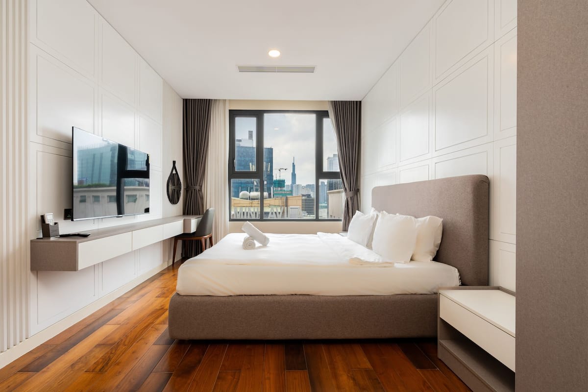 Une chambre d’hôtel moderne avec un grand lit, un téléviseur fixé au mur et une vue sur le panorama urbain par la fenêtre.