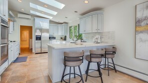 Una cocina moderna con una isla central, taburetes de bar y vistas al exterior.