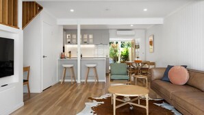 A modern interior with a kitchen, dining area, and living room, featuring wooden flooring, a cowhide rug, and a brown leather sofa. - Villa Le Miramar Perfect for your Pooch Holiday (Noosa)