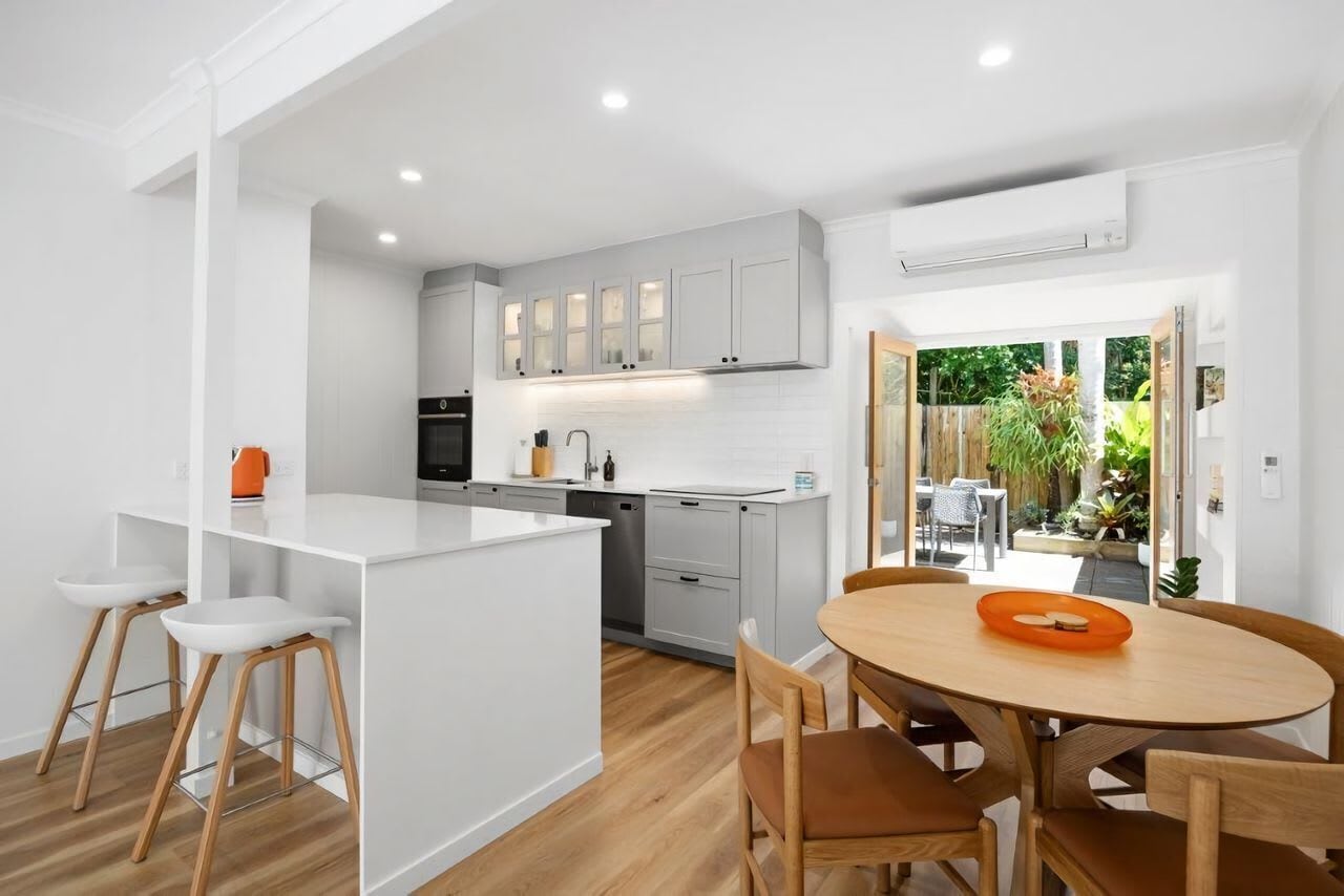 A modern kitchen with white cabinetry, a central island, and a dining area with wooden chairs and a table.