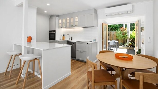 A modern kitchen with white cabinetry, a central island, and a dining area with wooden chairs and a table. - Villa Le Miramar Perfect for your Pooch Holiday (Noosa)